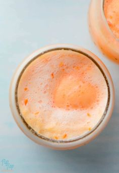 two glasses filled with orange juice sitting on top of a blue countertop next to each other