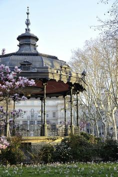 a gazebo surrounded by trees and flowers on a sunny day