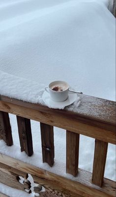 a cup of coffee sitting on top of a wooden bench covered in snow