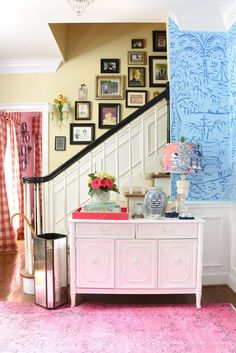 a pink rug in front of a white dresser with pictures on the wall behind it