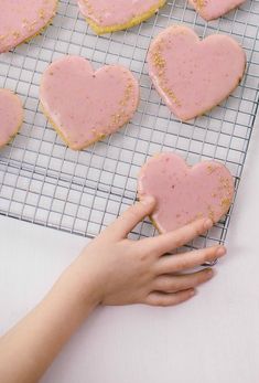 a person holding a heart shaped cookie on top of a cooling rack with pink frosting