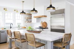 a kitchen with white counter tops and wooden chairs in front of an island that has four pendant lights hanging from the ceiling