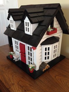 a doll house with red doors and windows on top of a wooden table next to a wall