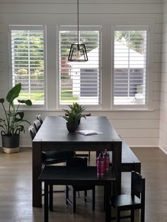 a dining room table and chairs in front of two windows with shutters on them