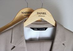 two wooden hangers are attached to a tan suit jacket with black label on it