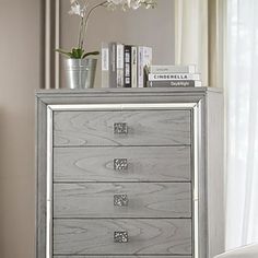 a silver chest of drawers sitting next to a window with white flowers on top of it