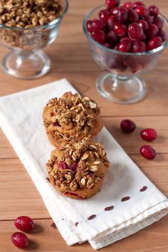 two muffins with cranberries and nuts are on a napkin next to a bowl of cherries