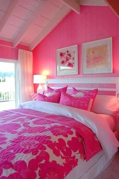 a bedroom with pink and white bedding, pictures on the wall, and two lamps