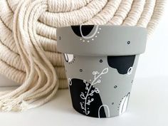 a white and black cup sitting next to a ball of yarn on top of a table