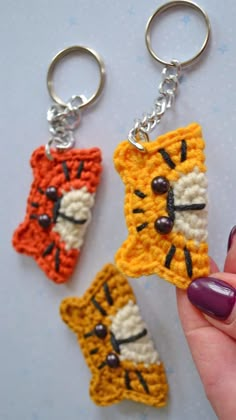 three crocheted keychains with cats on them, one is orange and the other is yellow