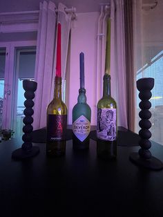 three wine bottles sitting on top of a table next to each other in front of a window