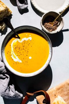 a bowl of carrot soup on a table with bread and other food items around it