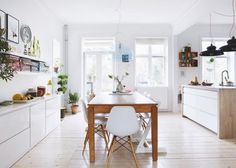 a dining room and kitchen with white walls, wood floors and wooden table surrounded by chairs