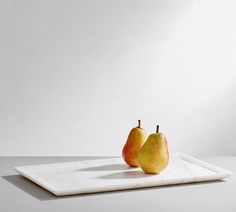 two pears are sitting on a white tray