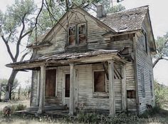 an old run down house sitting in the middle of a field with trees around it