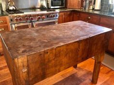 an old wooden kitchen island in the middle of a hardwood floored kitchen with stainless steel appliances