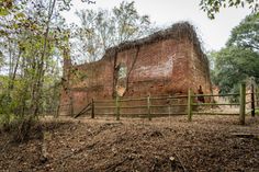 an old brick building in the woods with trees around it and a fence surrounding it