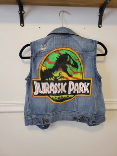 Hand painted Fandom denim vest with Jurassic Park logo. Ford color scheme vest in xs small. Cotton Grunge Denim Vest For Spring, Fitted Grunge Vest For Fall, Fitted Cotton Vest For Streetwear, Cotton Vest With Graphic Print For Spring, Casual Vest With Graphic Print For Fall, Y2k Cotton Denim Vest For Spring, Casual Graphic Print Vest For Fall, Y2k Style Cotton Denim Vest For Spring, Casual Festival Vest With Pockets