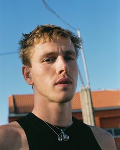 a young man wearing a black shirt standing in front of a building and looking at the camera