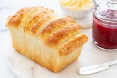 a loaf of bread sitting on top of a white plate next to a jar of jam