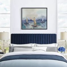 a bed in a bedroom next to two windows with sailboats on the water behind it