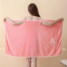 a woman is holding a pink towel with her back turned to the camera and she's standing in front of a white chair