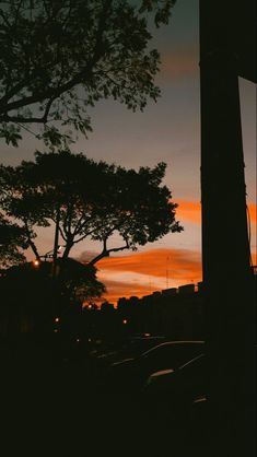 the sun is setting behind some trees and cars