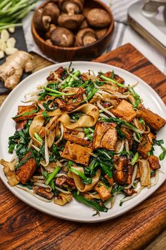 a white plate topped with lots of food on top of a wooden table next to vegetables