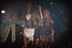 two women standing in front of a group of confetti on a black background