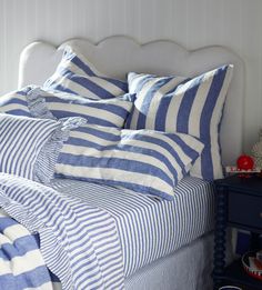 a bed with blue and white striped comforters on top of it, next to a night stand