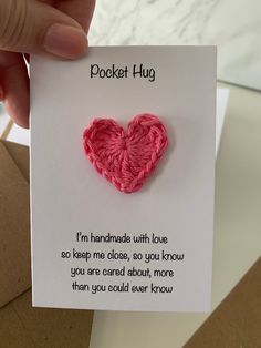 a person holding up a card with a crochet heart on it that reads pocket hug i'm handmade with love so keep me close, so you know you are caring about more than you