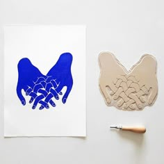 two hands holding each other on top of a piece of paper next to a paintbrush