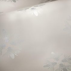 the wall paper is white and has silver flowers on it, with bees flying over them