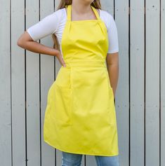 a woman wearing an apron standing in front of a wooden fence with her hands on her hips