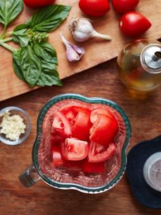 tomatoes and basil in a blender on a wooden cutting board next to garlic, pepper, and seasoning