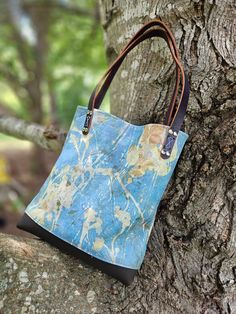 "Lovely, one of a kind handbag! Designed with leaves and plants ecoprinted onto Leather! Hand crafted  in my NC studio. This unique pale blue handbag showcases my ecoprinted (botanical) designs on both the exterior and interior of the bag. I combined it with a rich brown leather as a contrast on the boxed bottom, and two 1/2\" wide handles. The bag is 12\" high x 11\" wide by 3\" deep. It's a perfect size for carrying your essentials.  Handcrafted by me and finished with stylish silver rivets. Can be carried over the arm or ticked up under the shoulder. I ecoprint on both fabric and leather and the results are one of a kind. I collect various leaves and foliage from my NC farm and through a natural process, imprint them onto leather. I handcraft the hides into handbags, journals, accessori Artisan Blue Tote Bag, Artistic Blue Bag For Everyday Use, Artistic Blue Bags For Everyday, Hand Painted Blue Leather Bags, Artistic Blue Shoulder Bag For Everyday Use, Artistic Blue Shoulder Bag, Handmade Nature-inspired Travel Bag, Hand Painted Satchel Bag For Everyday Use, Hand Painted Tote Shoulder Bag For Everyday