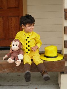 a young boy sitting on a porch with a stuffed monkey and yellow hat in front of him