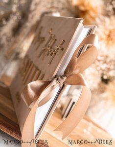 an open book with a ribbon tied around it on top of a wooden table next to flowers