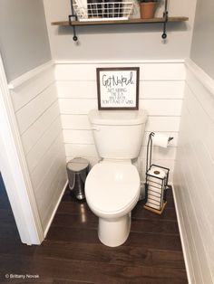 a white toilet sitting inside of a bathroom next to a wooden shelf filled with items