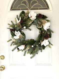 a christmas wreath on the front door with white flowers and pine cones hanging from it