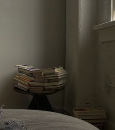 a stack of books sitting on top of a bed next to a window in a room