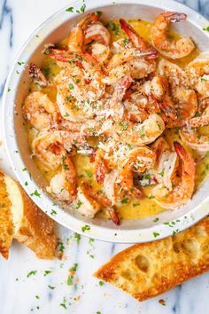 a white bowl filled with shrimp and garlic bread next to two slices of toasted bread