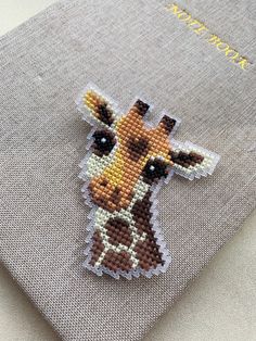 a cross - stitch giraffe brooch sits on top of a gray cloth