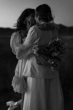 black and white photograph of two women hugging each other in front of the sun setting