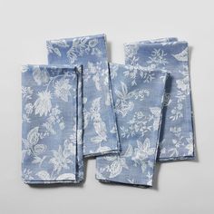 three blue napkins with white flowers on them sitting next to each other in front of a gray background