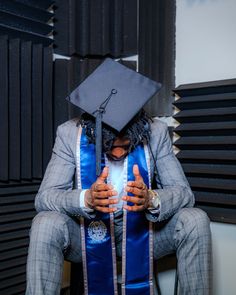 a man in a graduation cap and gown sitting down with his hands on his chest