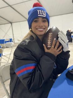 a woman holding a football in her right hand and wearing a new york giants hat