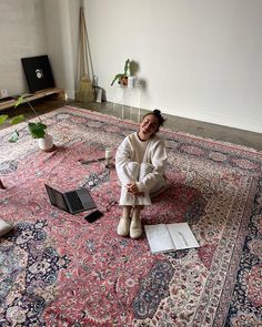 a woman sitting on top of a rug next to a laptop computer