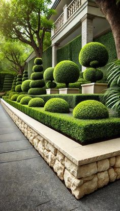 an outdoor garden with stone planters and green bushes in front of a house on a sunny day