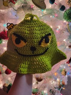 a green crocheted hat with a smiley face on it is held up in front of a christmas tree